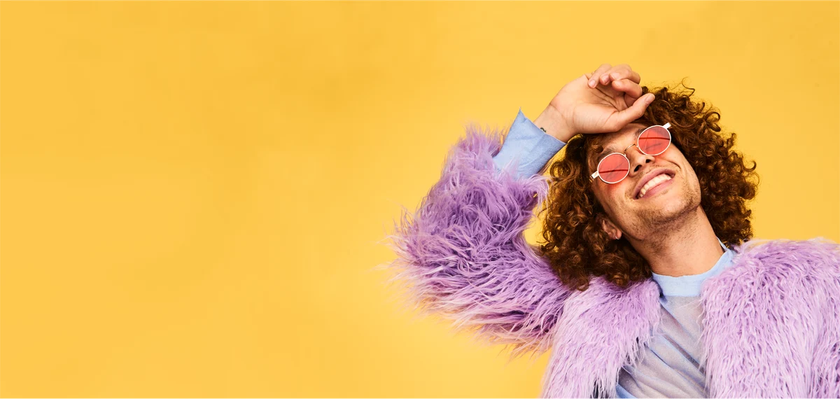 man with curly hair, sun glasses and furry purple coat is smiling